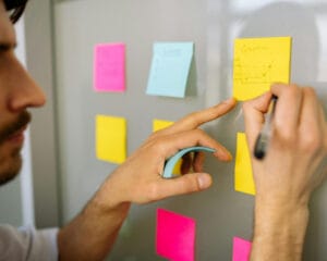 Person writing on sticky notes on a board.