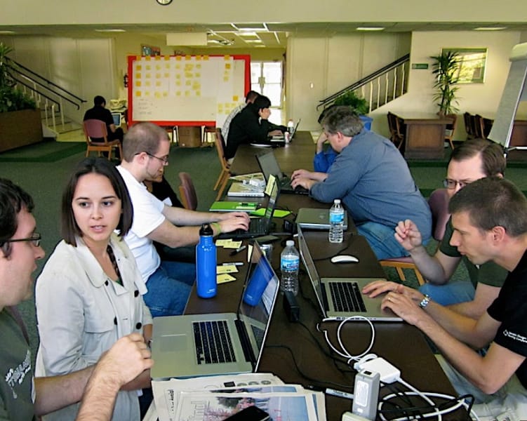 Team collaborating in office with laptops and notes.